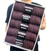 A box displaying five skeins of purple alpaca wool yarn for knitting and crochet projects.