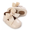 A pair of light beige lace-trimmed baby girl moccasin shoes with bows.