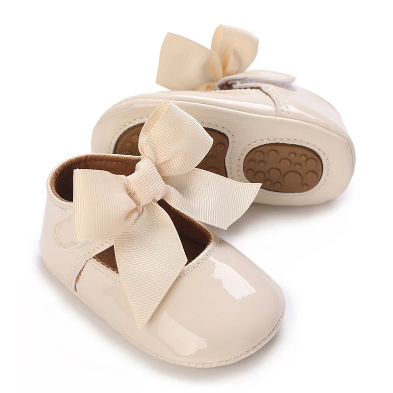 A pair of light beige lace-trimmed baby girl moccasin shoes with bows.