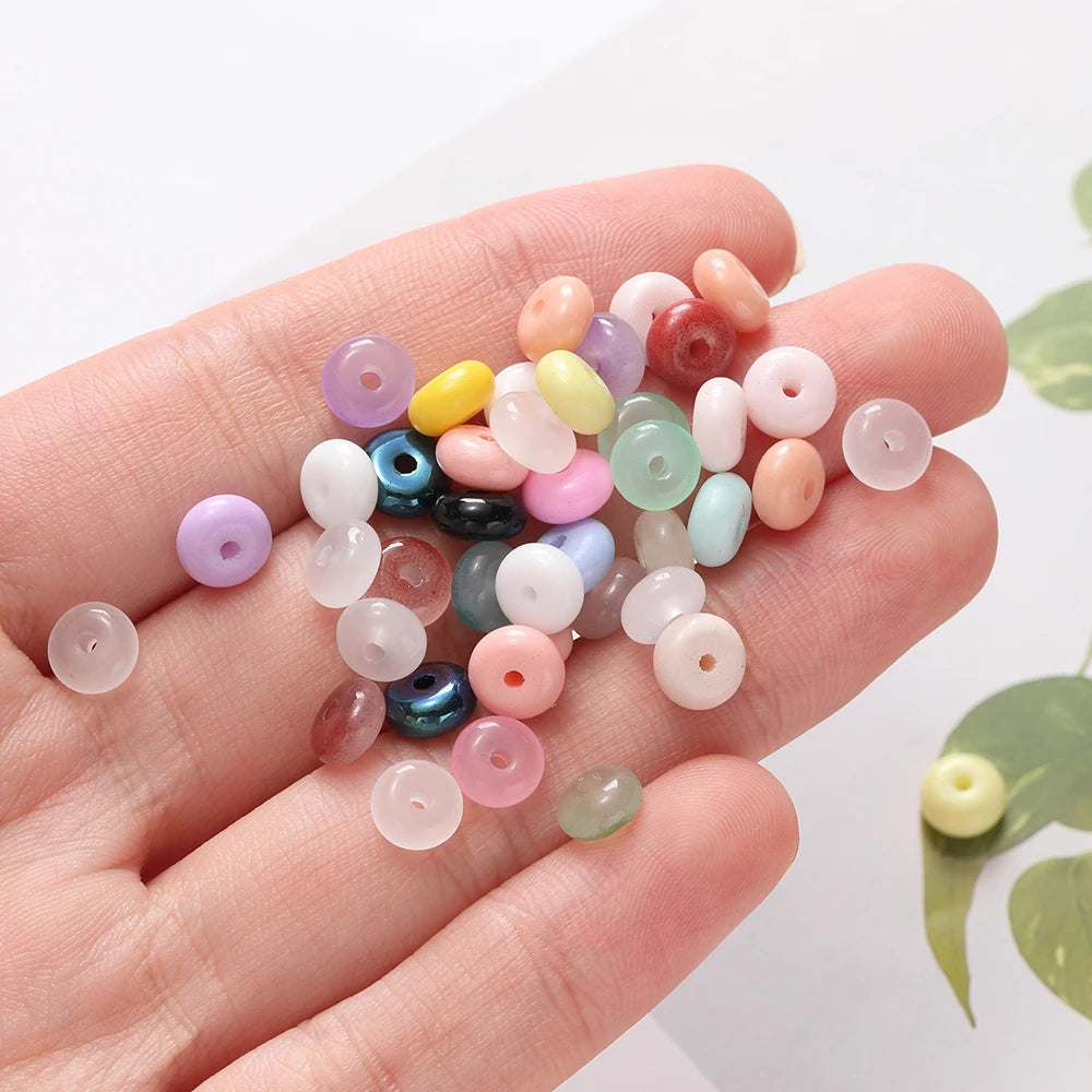 A hand holds a collection of small, round imitation jade glass spacer beads in various pastel and translucent colors.