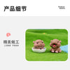 A pair of small, brown resin hippo figurines sitting on green grass.