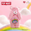 A pink Care Bear figurine with a rainbow design is displayed against a soft, fluffy background.
