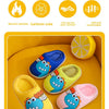 A hand is holding a pair of yellow and blue cartoon dinosaur plush slippers on a yellow surface.