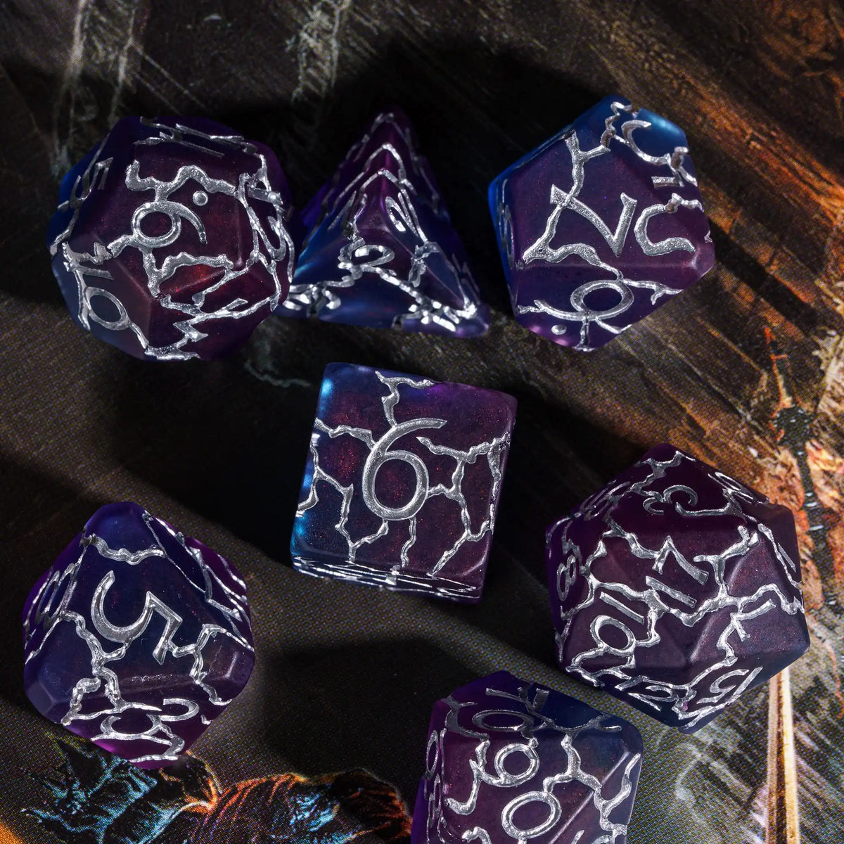 A set of seven frosted crack resin polyhedral dice in shades of purple and blue resting on a dark wooden surface.