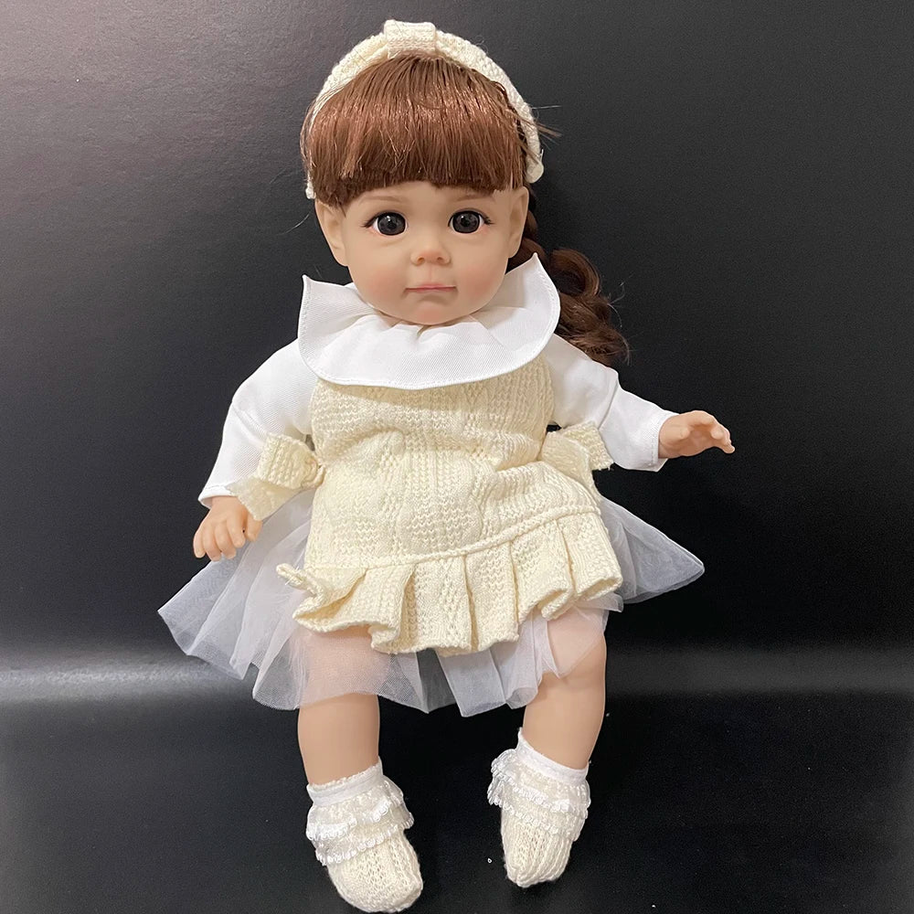 A lifelike 14-inch reborn baby doll with a white dress and bonnet, posed against a dark background.