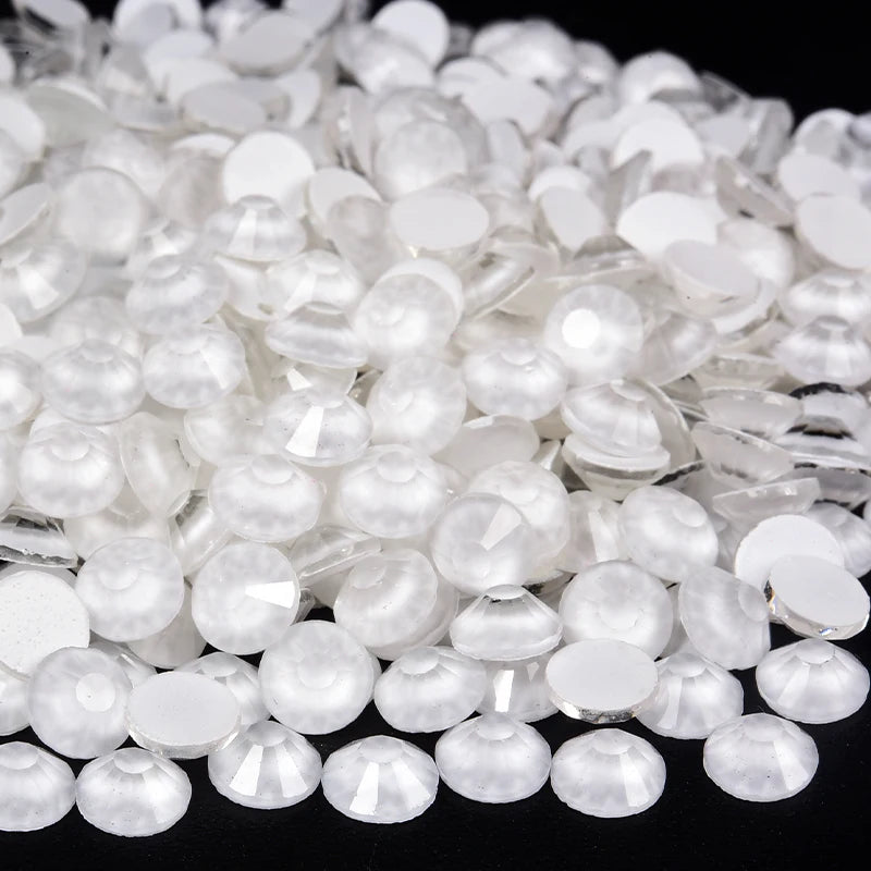 A close-up view of clear and white sparkling crystal flatback rhinestones scattered on a dark surface.