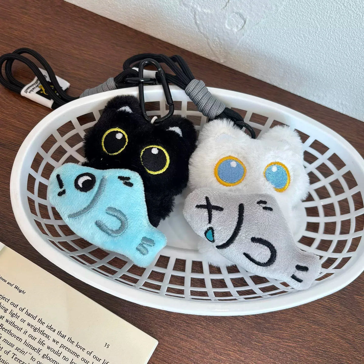 A cute plush black cat keychain charm with blue and white accents displayed in a white basket.