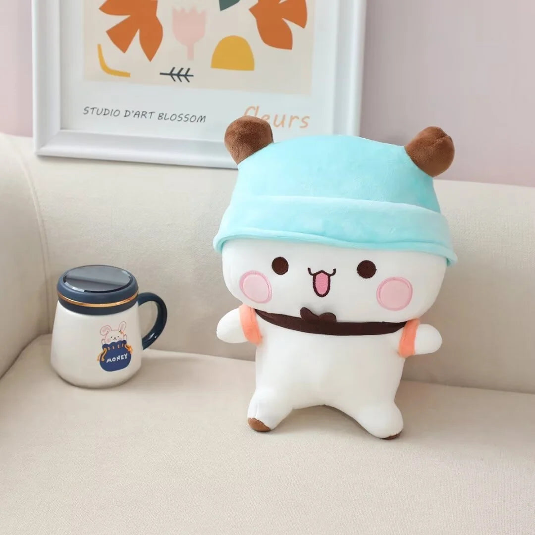 A white panda bear plush toy wearing a light blue hat and brown collar sitting on a sofa.