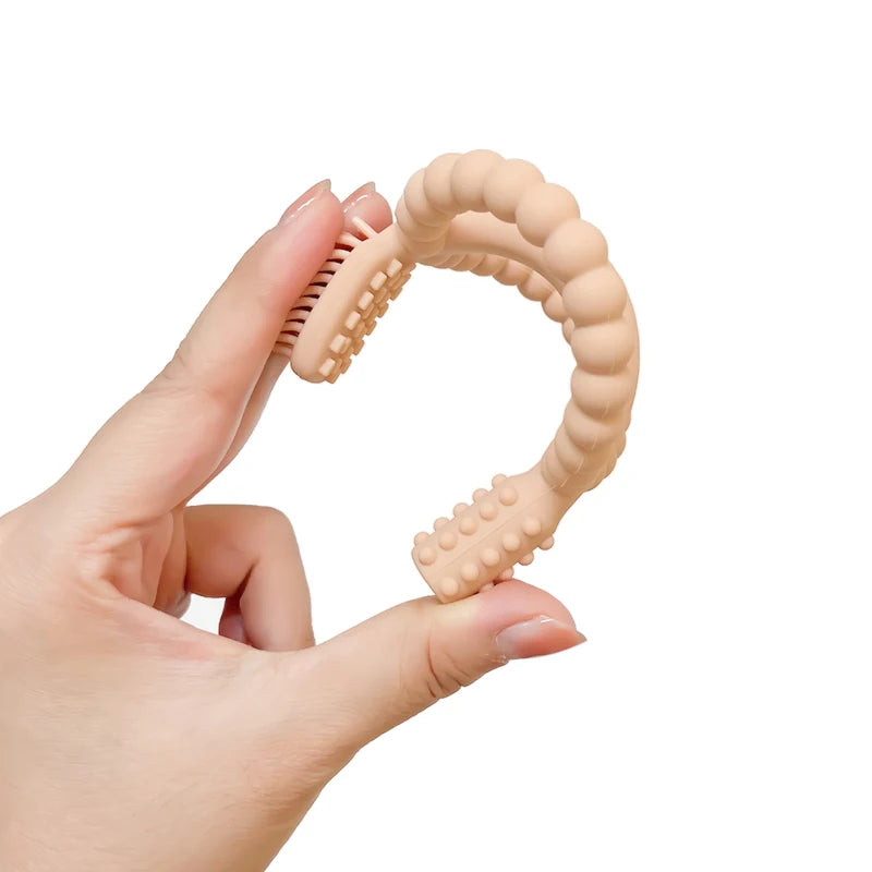 A hand is holding a beige silicone baby teether with textured grips.