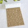 A roll of floral texture material for polymer clay and crafting is placed on a white surface.