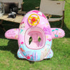 Pink inflatable aircraft swim ring with a yellow control wheel and tropical designs on green grass.