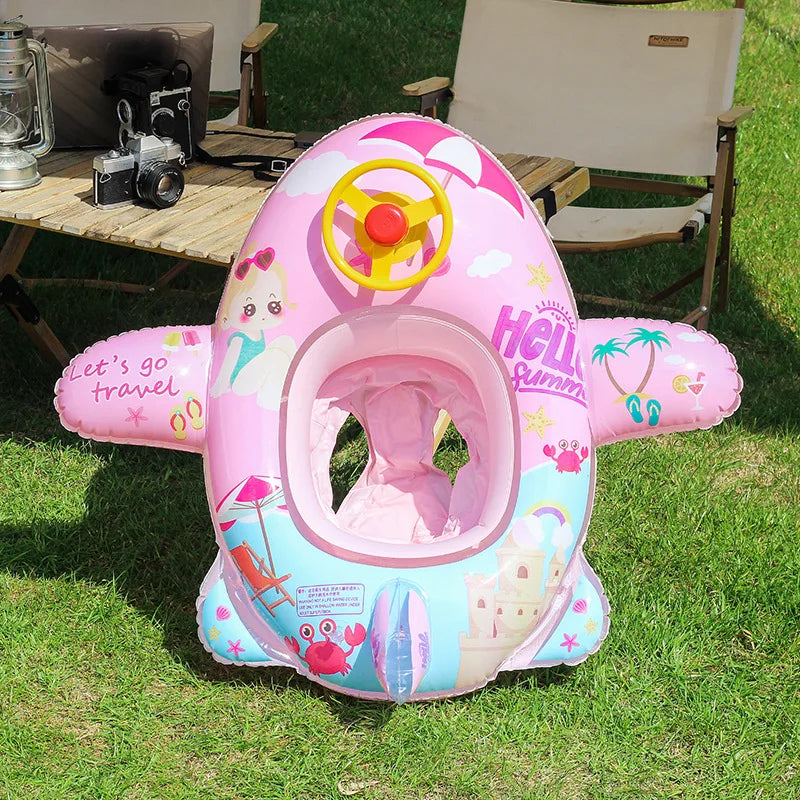 Pink inflatable aircraft swim ring with a yellow control wheel and tropical designs on green grass.