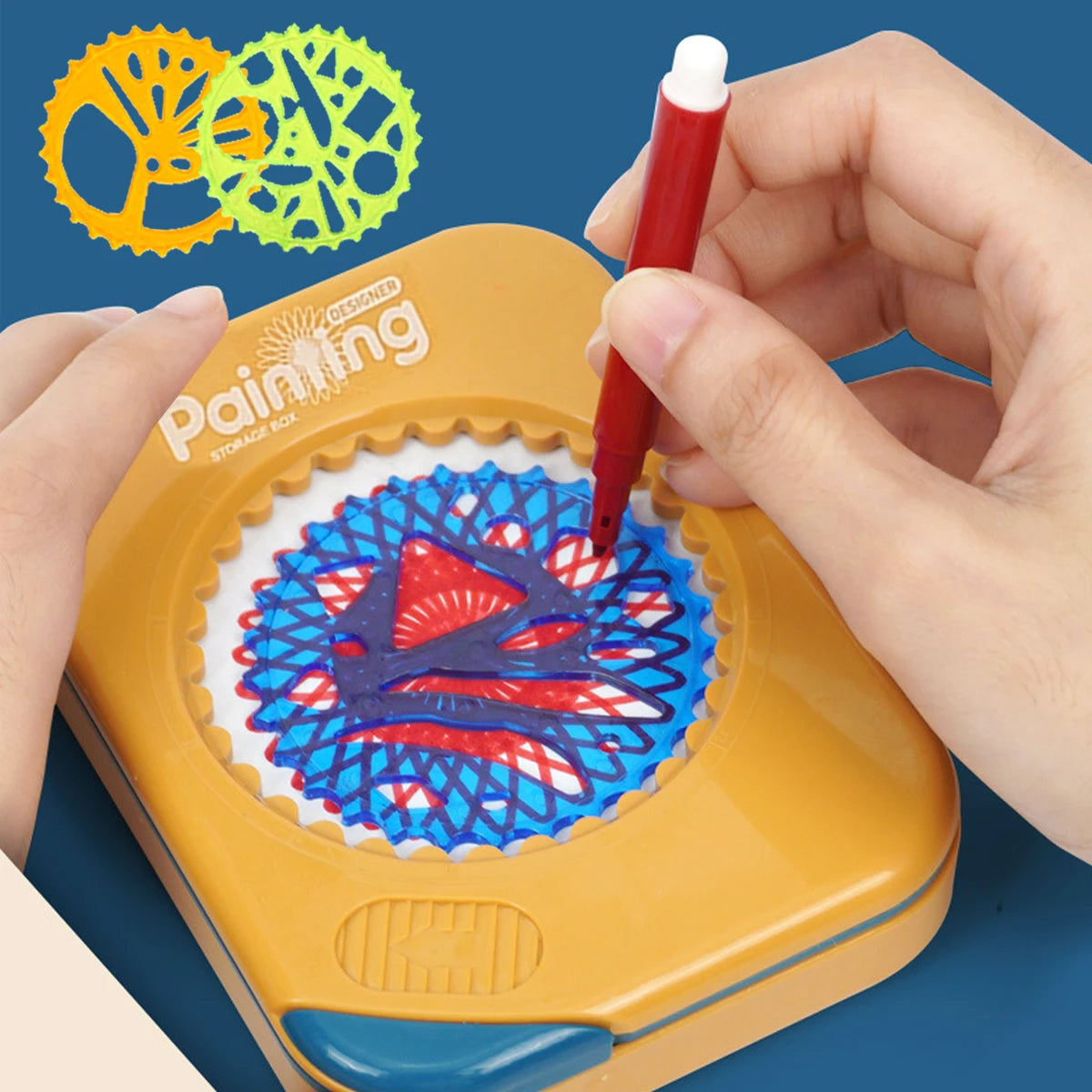 A hand is using a red paintbrush to draw a colorful design onto a yellow storage box featuring geometric templates.
