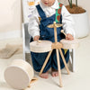 A toddler is sitting in a chair with a wooden drum set, featuring various sized wooden drums and mallets.