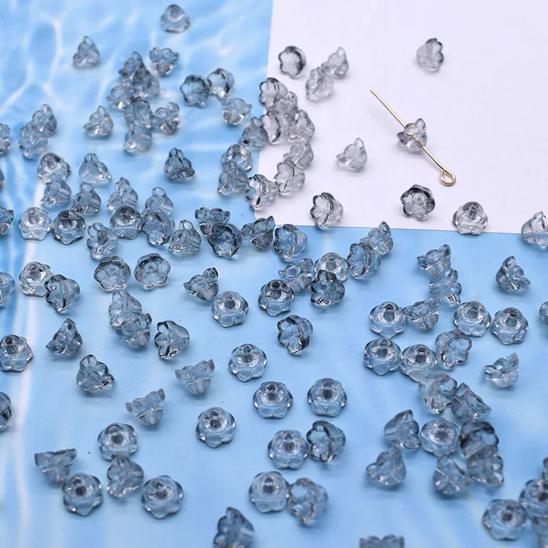 A collection of clear blue glass beads shaped like lily of the valley flowers scattered on a white background.