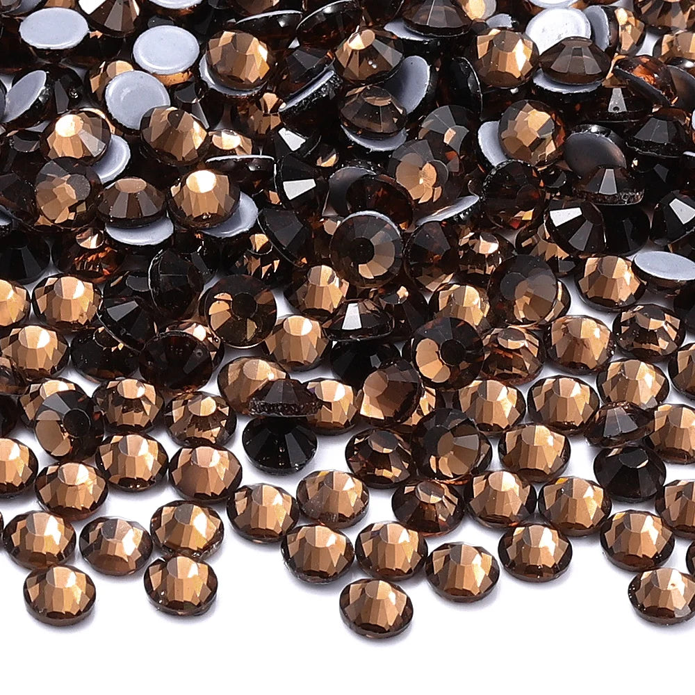 A close-up view of dark brown and amber glass crystal hot fix rhinestones scattered on a white background.