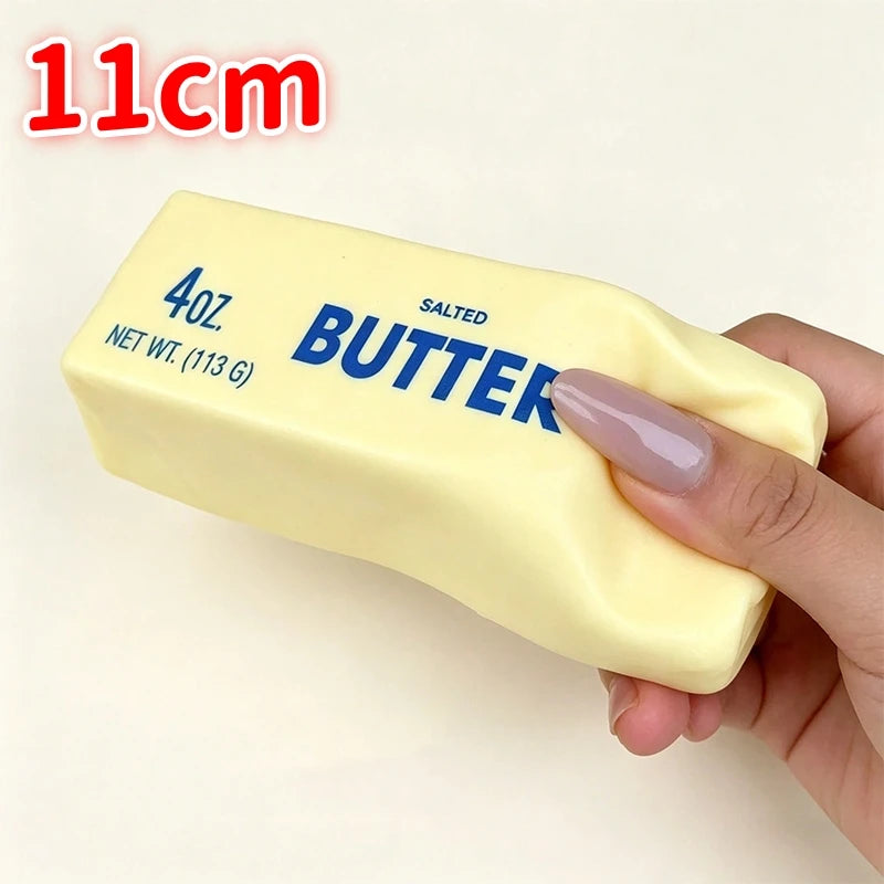 A hand holds a yellow salted butter stick fidget toy labeled 4oz net wt 113g.