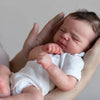 A newborn baby with hand-rooted hair is being held by a person.