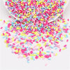 A pile of colorful polymer clay slice sprinkles in various shades of pink, purple, and yellow scattered on a white surface.