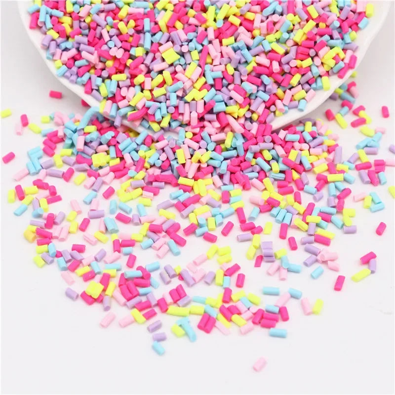 A pile of colorful polymer clay slice sprinkles in various shades of pink, purple, and yellow scattered on a white surface.