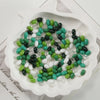 A white oval dish filled with various green and black glass rice grain beads for jewelry making