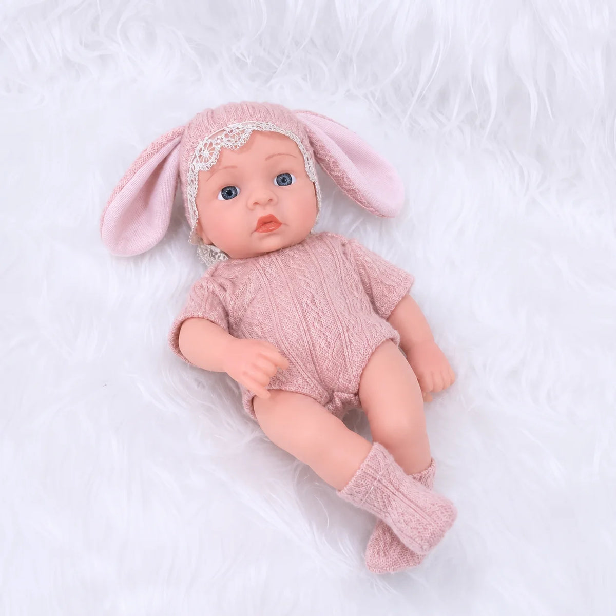 A realistic soft vinyl baby doll with a pink outfit and headband lying on white fluffy fur.