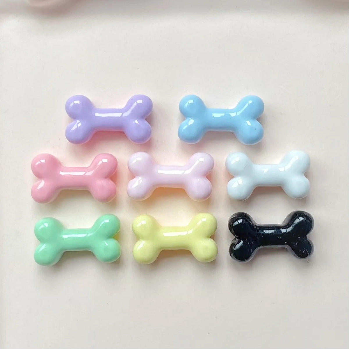 A collection of six small, colorful resin bone charms in various pastel and dark colors for nail art or jewelry making.