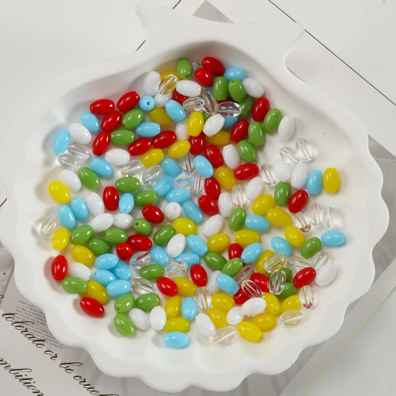 A variety of oval glass rice grain beads in red, green, yellow, white, and blue are displayed in a white dish.