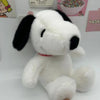 A white plush toy of Snoopy with black ears and nose sitting on a white surface.