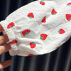 A close-up of a white long-sleeve shirt with a red strawberry print, held by a hand.