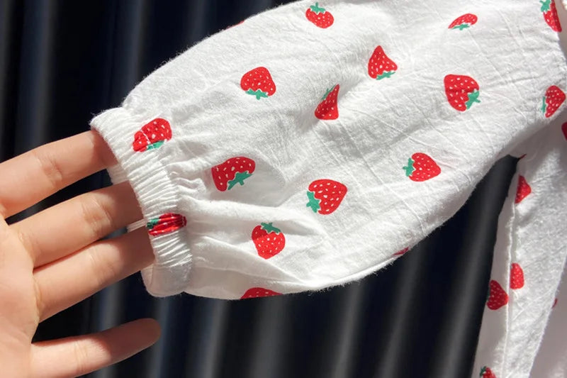 A close-up of a white long-sleeve shirt with a red strawberry print, held by a hand.
