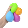 A hand is squeezing a stack of brightly colored stress relief balls, including lime green, orange, and blue.
