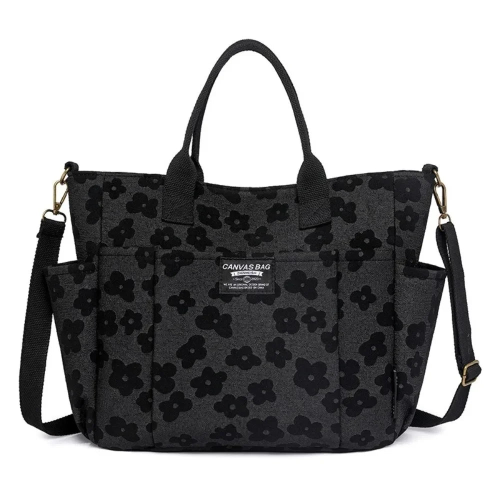 Black canvas tote bag with multiple pockets featuring a floral pattern.