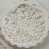 A white ceramic dish filled with oval glass rice grain beads for jewelry making