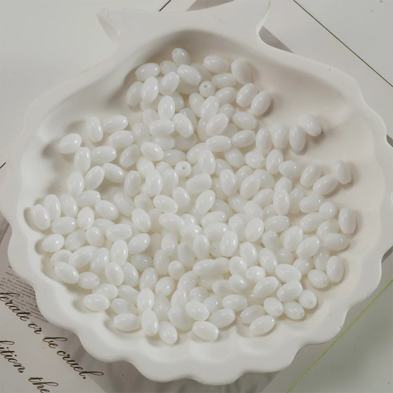 A white ceramic dish filled with oval glass rice grain beads for jewelry making
