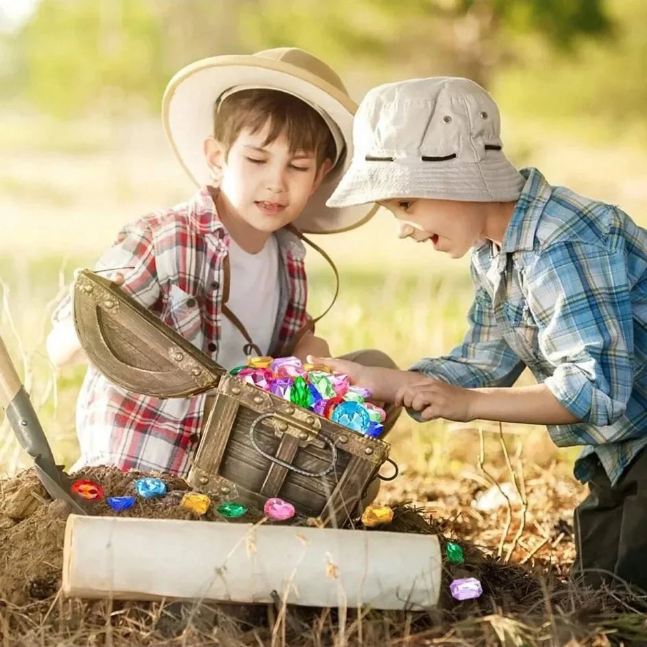 Two boys in hats digging for colorful acrylic gemstones in the dirt.