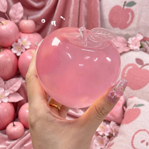 A hand holds a translucent pink apple-shaped sensory fidget ball surrounded by pink floral elements.