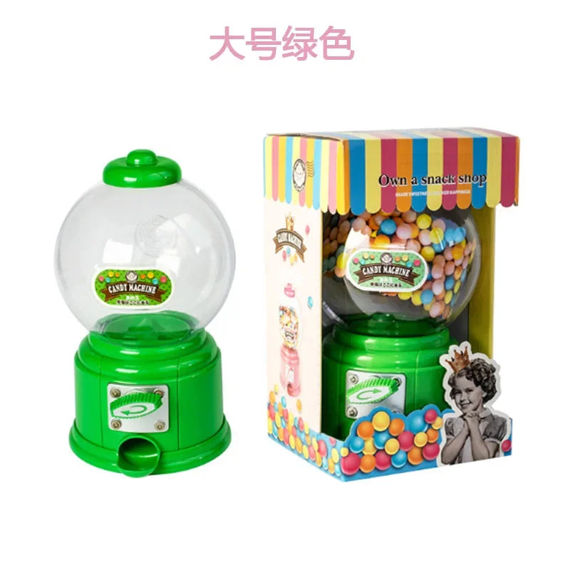 A green and pink kids candy dispenser with a clear dome and a box of colorful gumballs.