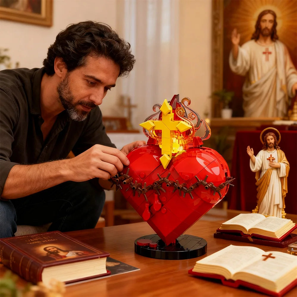 A red heart shaped building block set with a golden cross, placed on a wooden table next to open books.