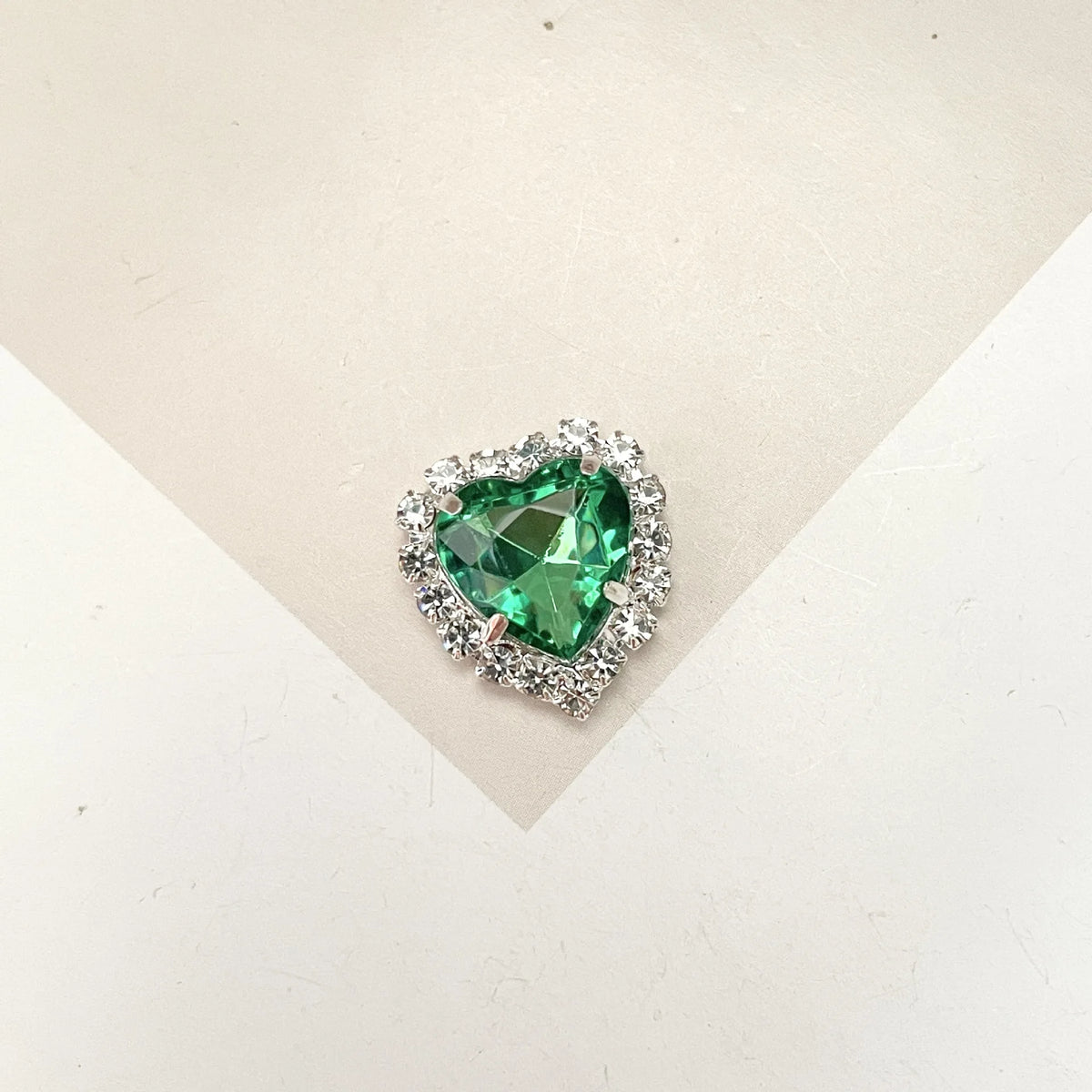 A brilliant green heart-shaped gemstone surrounded by clear rhinestones for DIY crafts.