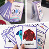 A hand holds a purple and white stack of English vocabulary flashcards featuring clothing items like shirts and sweaters.