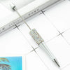 A silver ballpoint pen with a beaded tip is shown resting on a white surface next to a book.