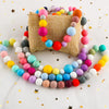 A string of colorful silicone beads in various sizes is displayed next to a burlap fabric, scattered with gold stars.