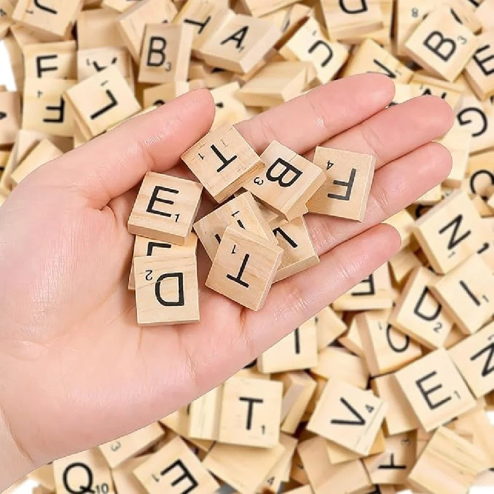 A hand holds several wooden alphabet letter tiles scattered among many more.