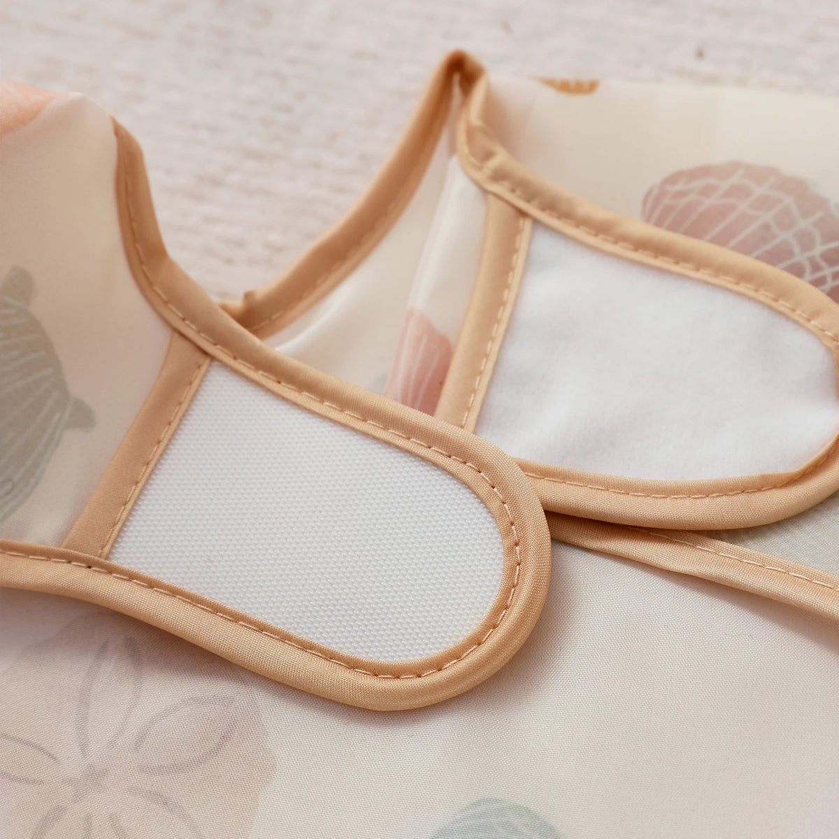 A pair of light beige waterproof baby bibs with long sleeves shown against a white background.