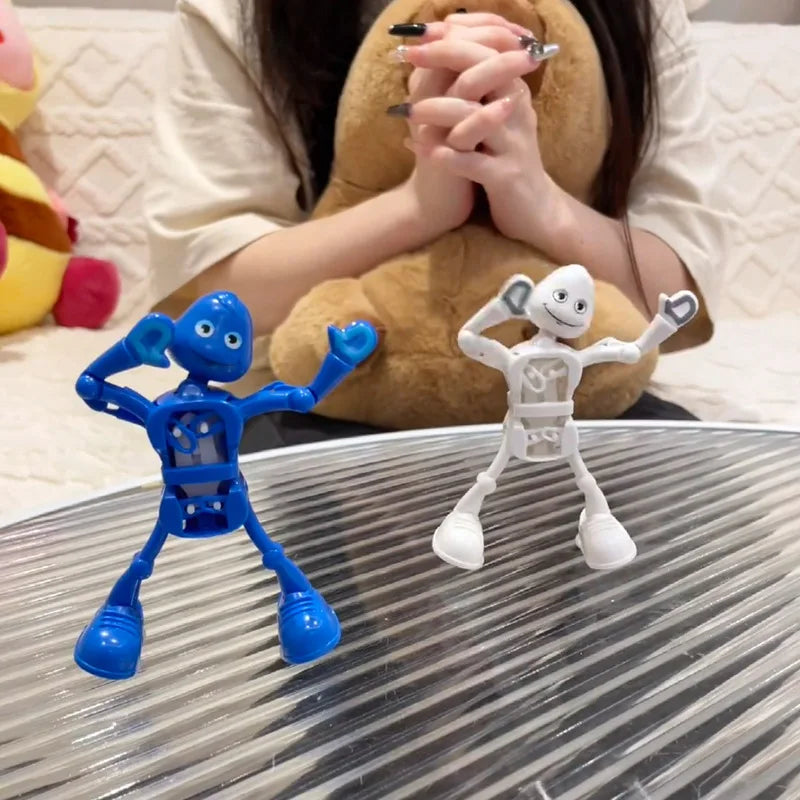 A blue wind-up dancing robot toy is displayed on a glass surface next to a white clockwork robot.