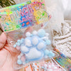 A clear plastic bag contains a light blue and pink squishy toy shaped like a cat paw, packaged for stress relief.