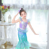 A young girl wearing a turquoise mermaid fantasy dress with a ruffled fishtail skirt and purple hair accessory.