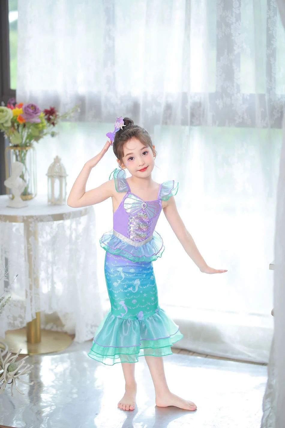 A young girl wearing a turquoise mermaid fantasy dress with a ruffled fishtail skirt and purple hair accessory.