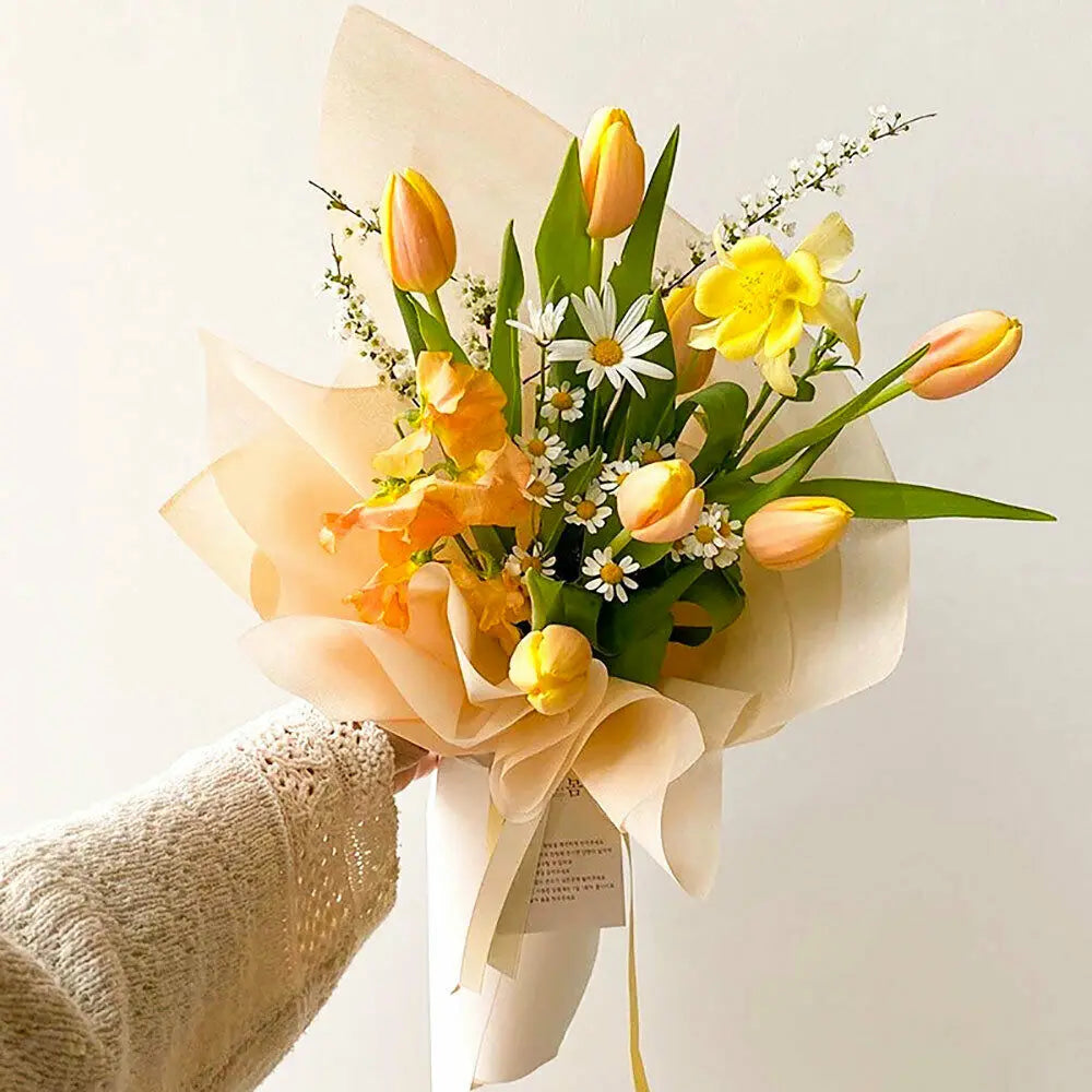 A bouquet of yellow and orange tulips and daisies wrapped in translucent tissue paper for gifting
